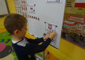 Chłopiec przywiesza na tablicy obrazki godła Polski, obliczając tym samym wynik dodawania.
